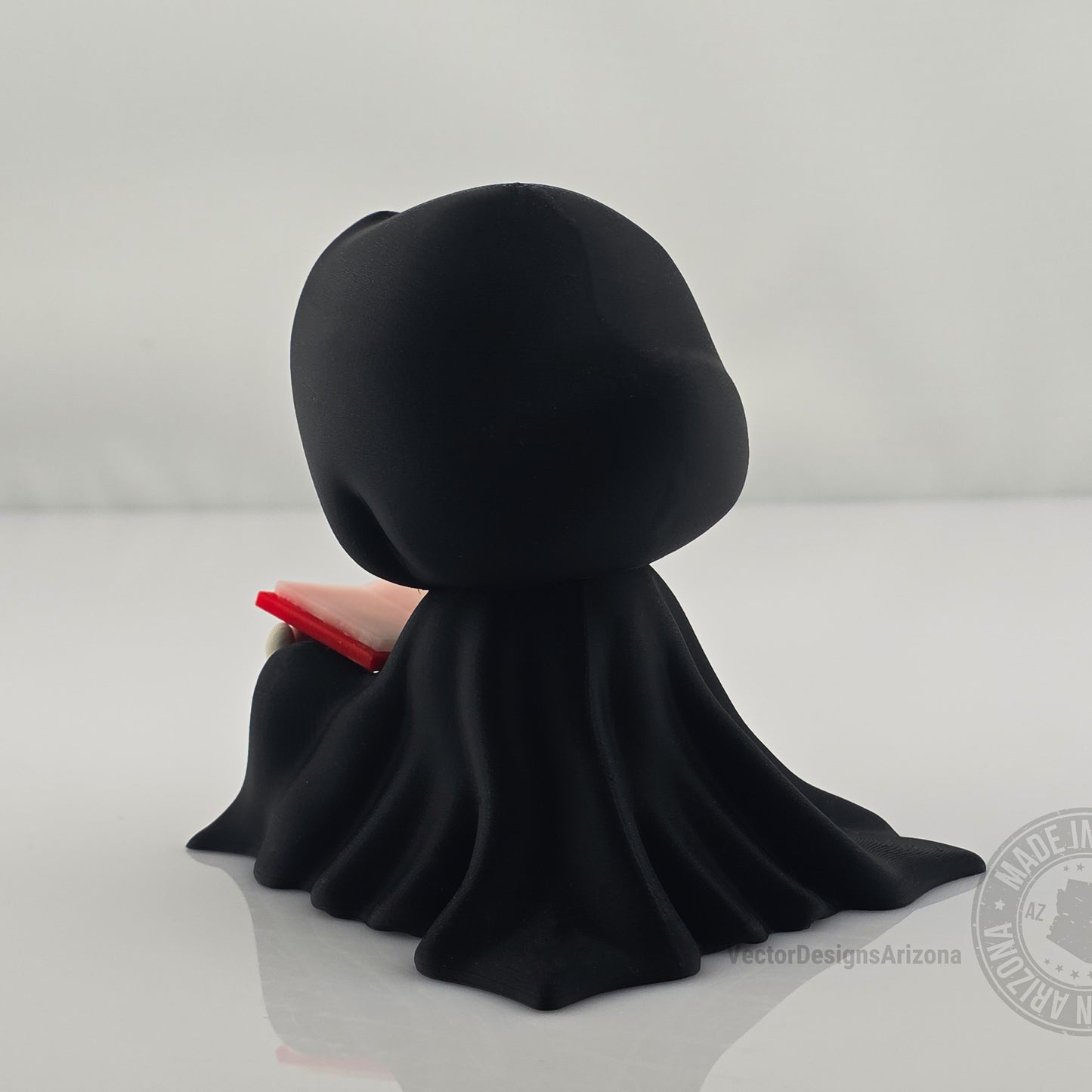 Back view of Grim Reaper figurine in a flowing black cloak holding a red book.