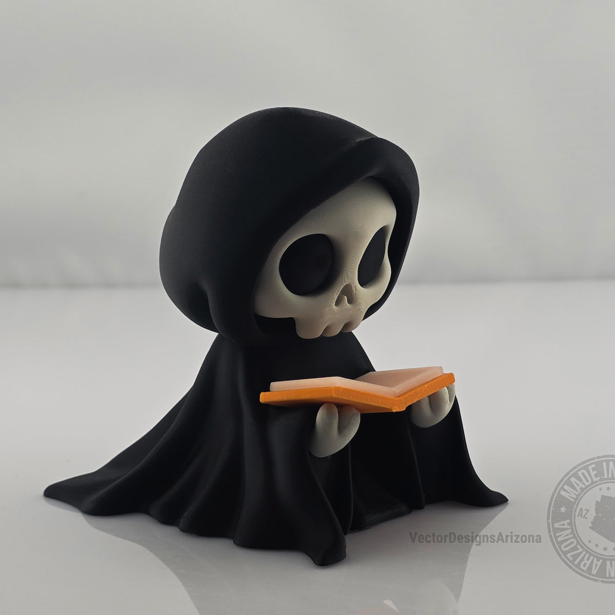 Cute grim reaper figurine holding orange-edged book on clean white background.
