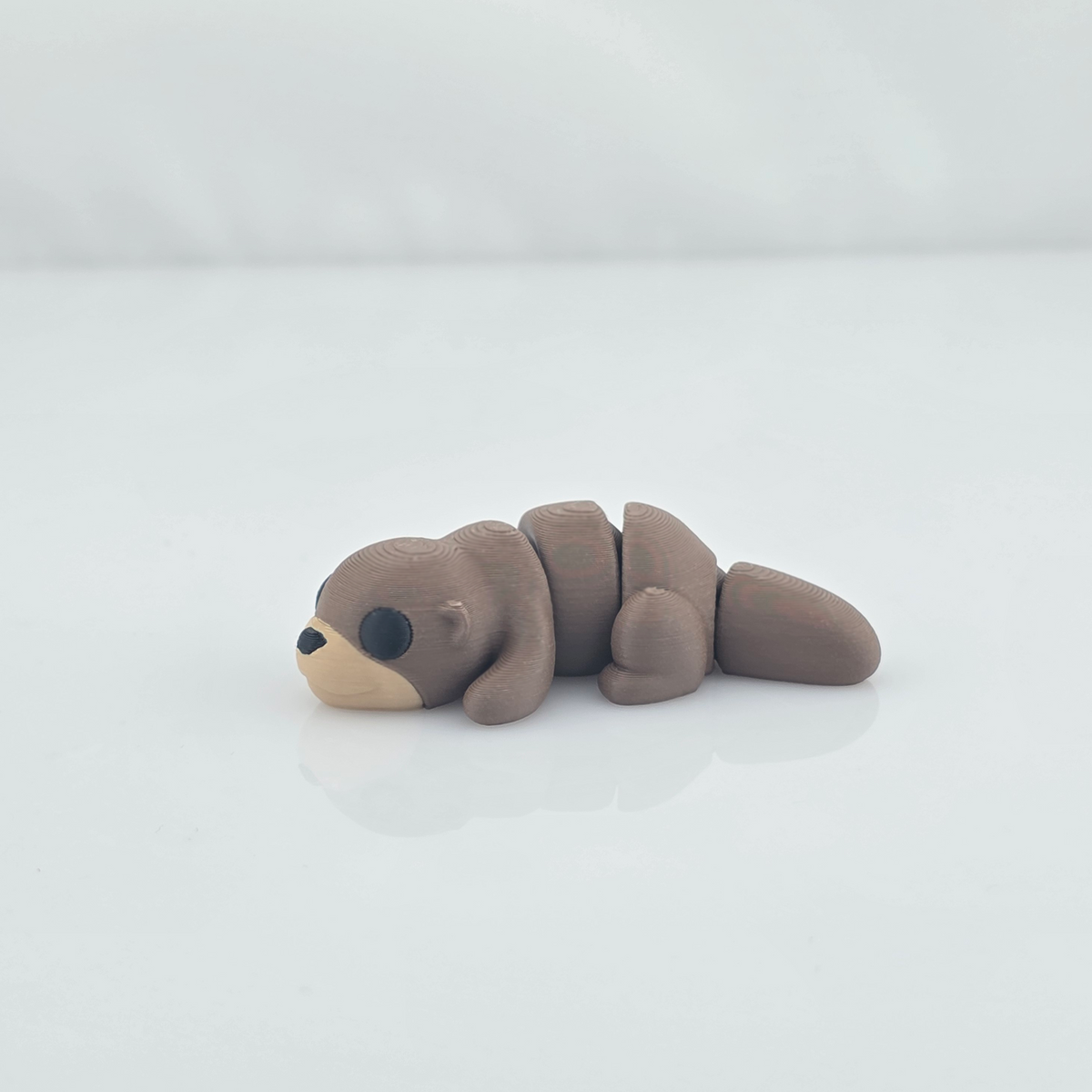 Mini flexy otter 3D printed figurine lying on white seamless background.