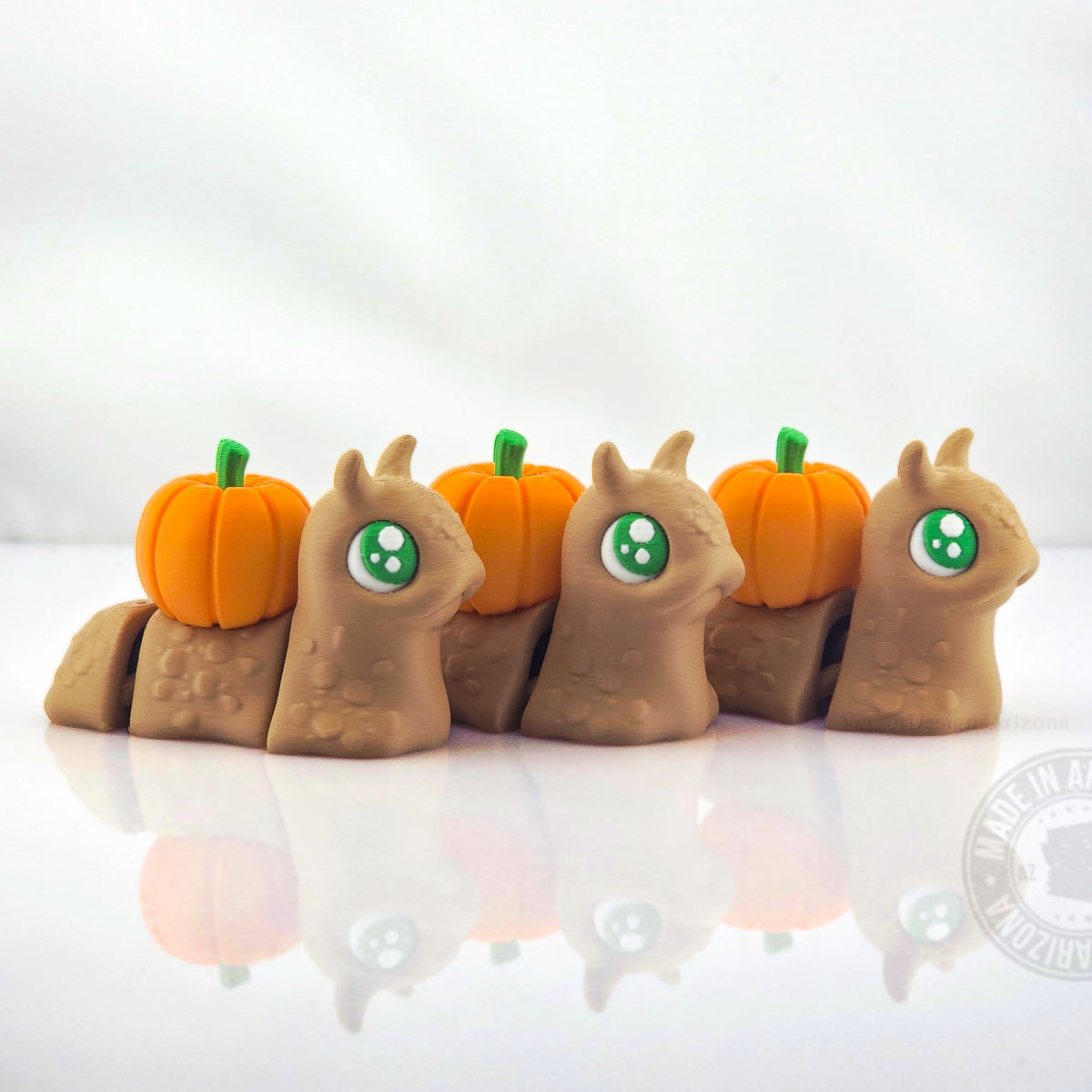 Row of tan spooky snails with bright orange pumpkin shells on white reflective background.