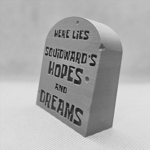 Angled gray tombstone desk sign showing engraved funny hopes and dreams text.