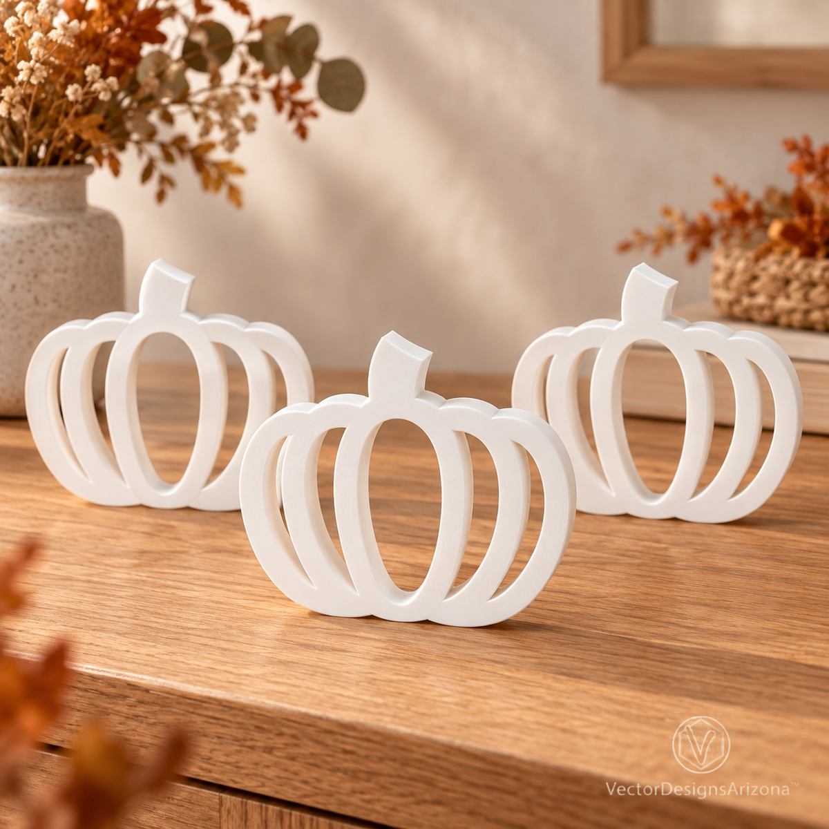 Three ivory white minimalist 3D-printed pumpkins with open-frame designs, styled on a wood console with warm fall decor.