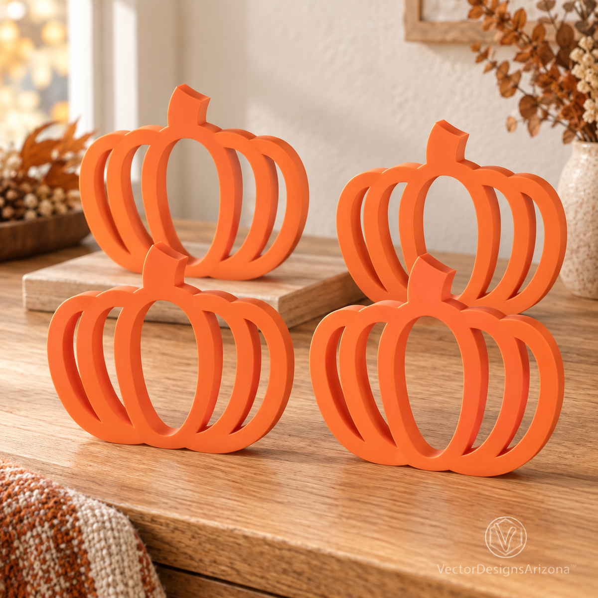 Four Mandarin orange minimalist 3D-printed pumpkins with open-frame designs, styled on a wood console with warm fall decor.