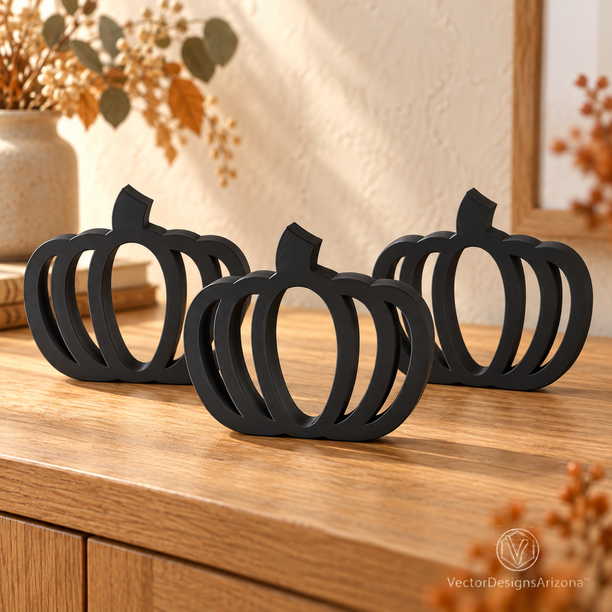 Three matte black minimalist 3D-printed pumpkins with open-frame designs, styled on a wood console with warm fall decor.