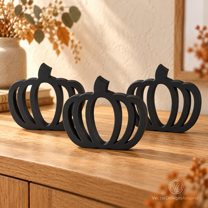 Three matte black minimalist 3D-printed pumpkins with open-frame designs, styled on a wood console with warm fall decor.