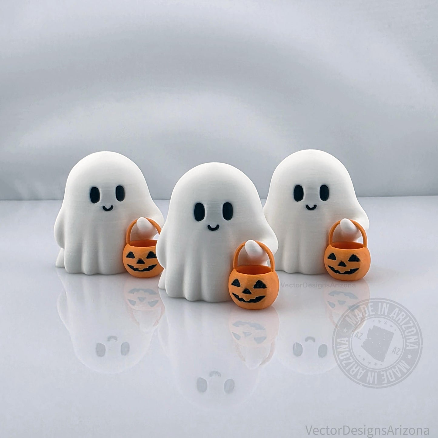 Set of three smiling ghost figurines, 3D printed in white PLA and holding orange trick-or-treat buckets, handmade Halloween decorations.