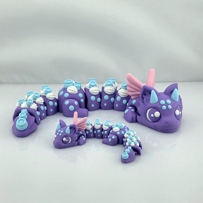 Large and mini Blueberry Dragon 3D printed flexi fidget toys posed together in a curved shape on a white surface.