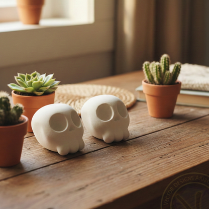 Two white cartoon skull figurines on wooden desk with small potted succulents nearby.