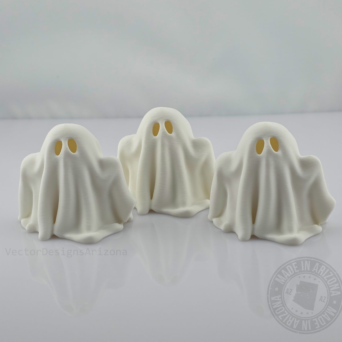 Three minimalist white ghost figurines on glossy white background, front view.