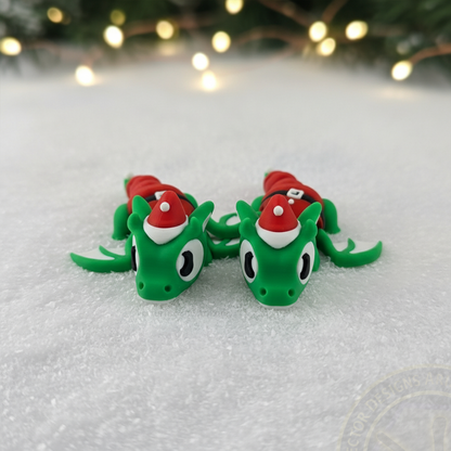 Pair of VectorDesignsArizona 3D printed flexi Elf Dragon figurines on snow with soft holiday lights in the background.