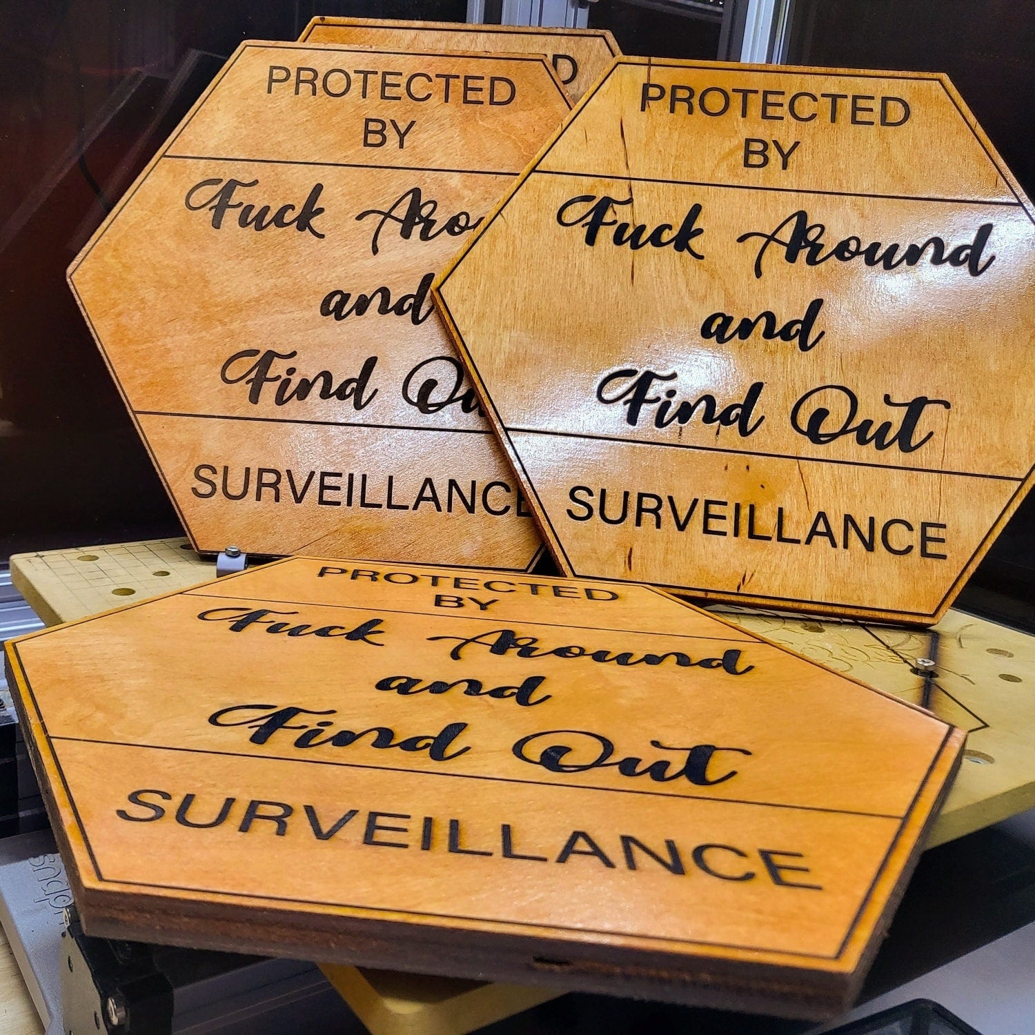 Several FAFO surveillance wood signs stacked on a workshop table with warm lighting.