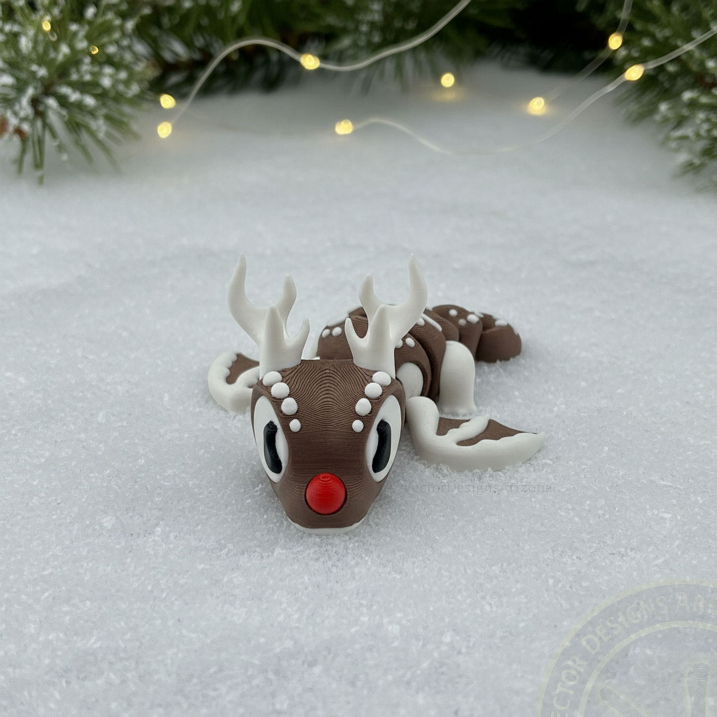 Front view of a VectorDesignsArizona 3D printed flexi Reindeer Christmas figurine on snow with pine greenery and warm string lights.