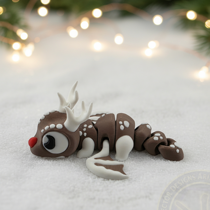 Side view of a VectorDesignsArizona 3D printed flexi Reindeer figurine resting on snow with blurred holiday lights in the background.