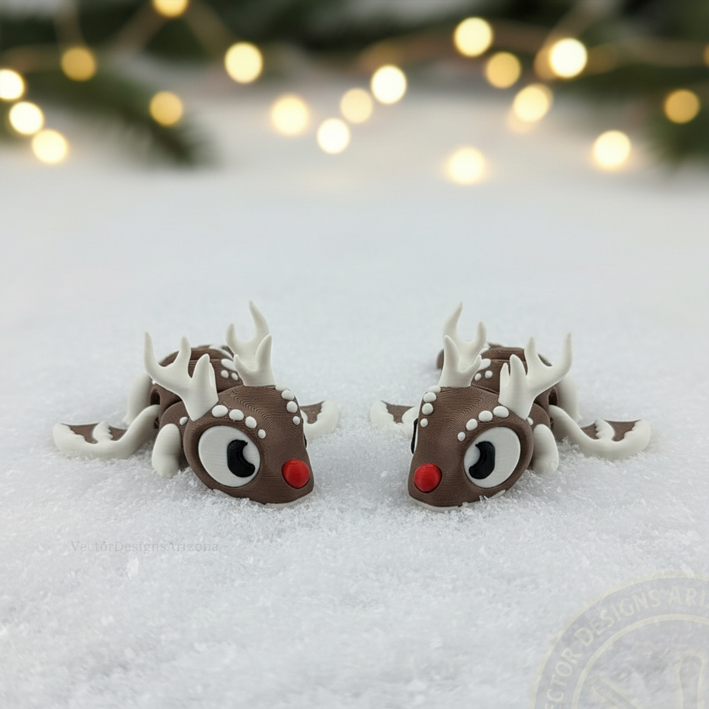 Pair of VectorDesignsArizona 3D printed flexi Reindeer figurines on snow with soft-focus holiday lights and pine branches behind them.