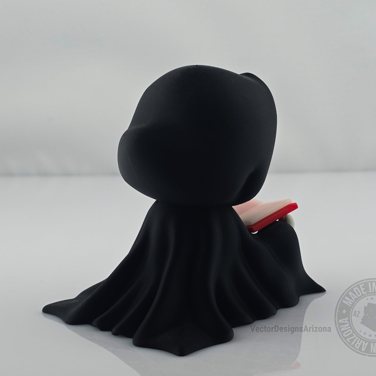 Back side view of cute grim reaper figurine reading a red-edged book.