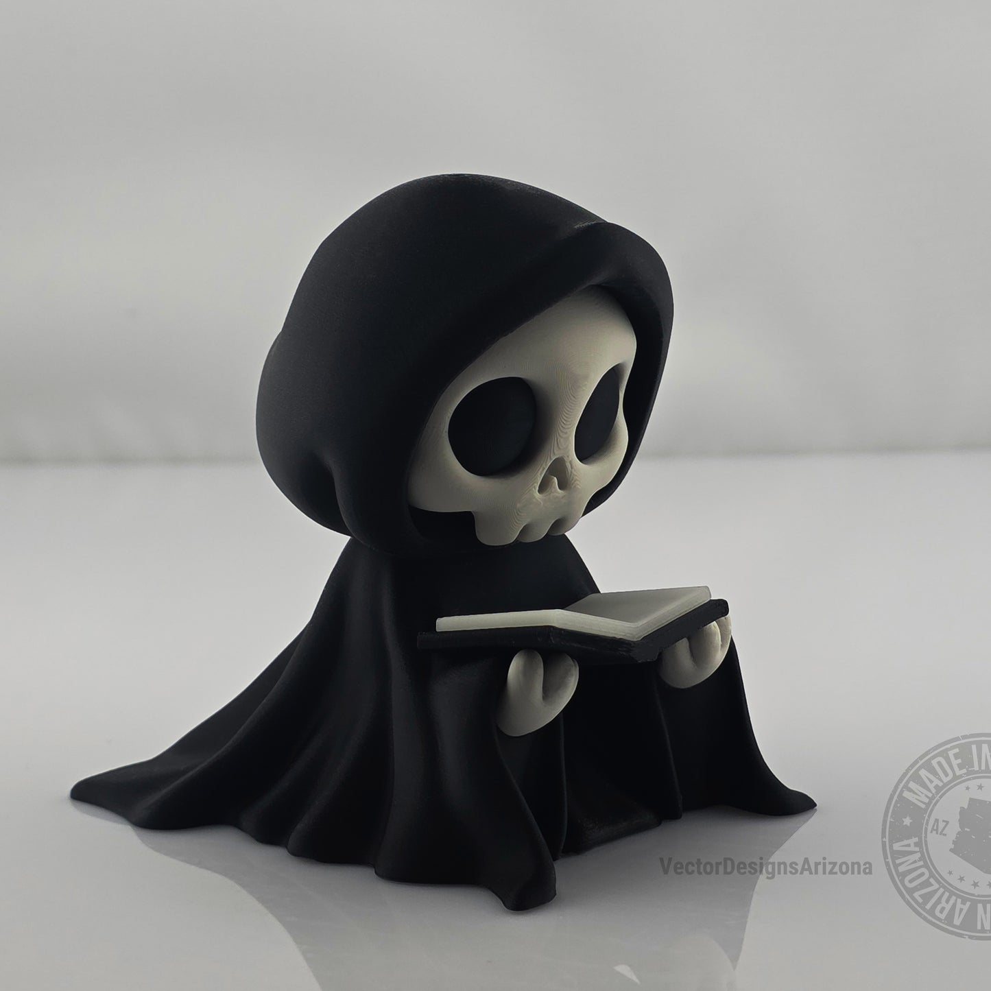 Cute grim reaper figurine holding black-edged book on clean white background.