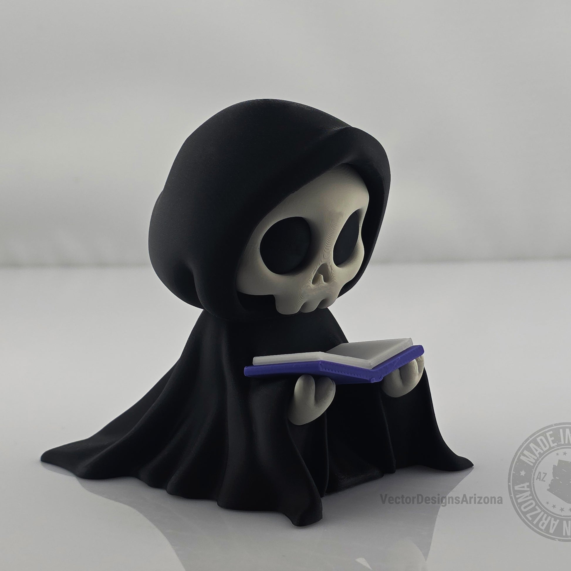 Cute grim reaper figurine holding blue book on clean white background.