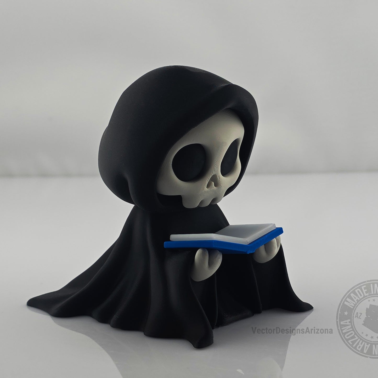 Cute grim reaper figurine holding blue-edged book on clean white background.