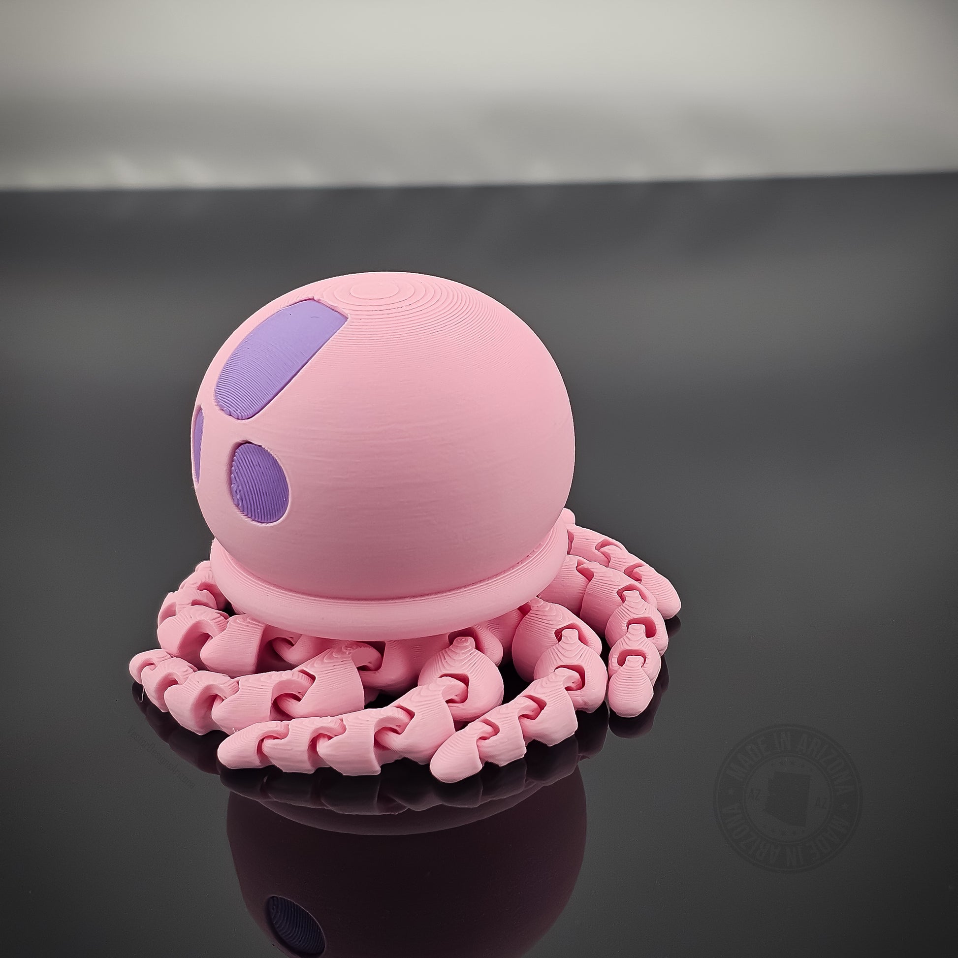 Pink jellyfish flexi fidget toy with tentacles curled beneath it on glossy surface.