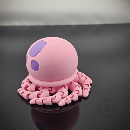 Pink jellyfish flexi fidget toy with tentacles curled beneath it on glossy surface.