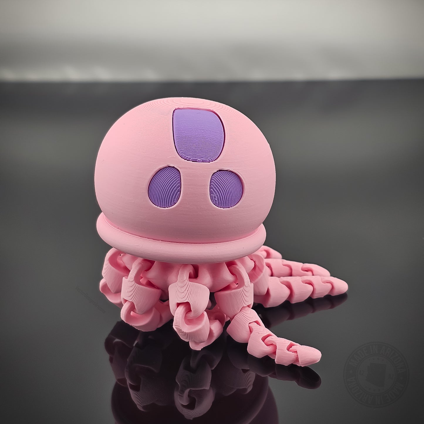 Pink jellyfish flexi fidget toy with articulated tentacles on glossy reflective surface.
