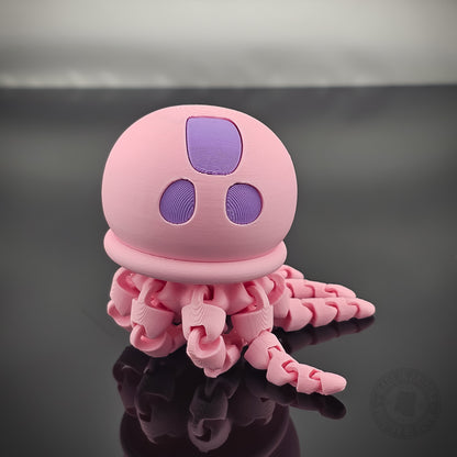 Pink jellyfish flexi fidget toy with articulated tentacles on glossy reflective surface.