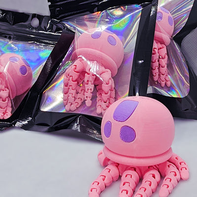 Pink jellyfish flexi fidget figurine in front of holographic packaged jellyfish toys.