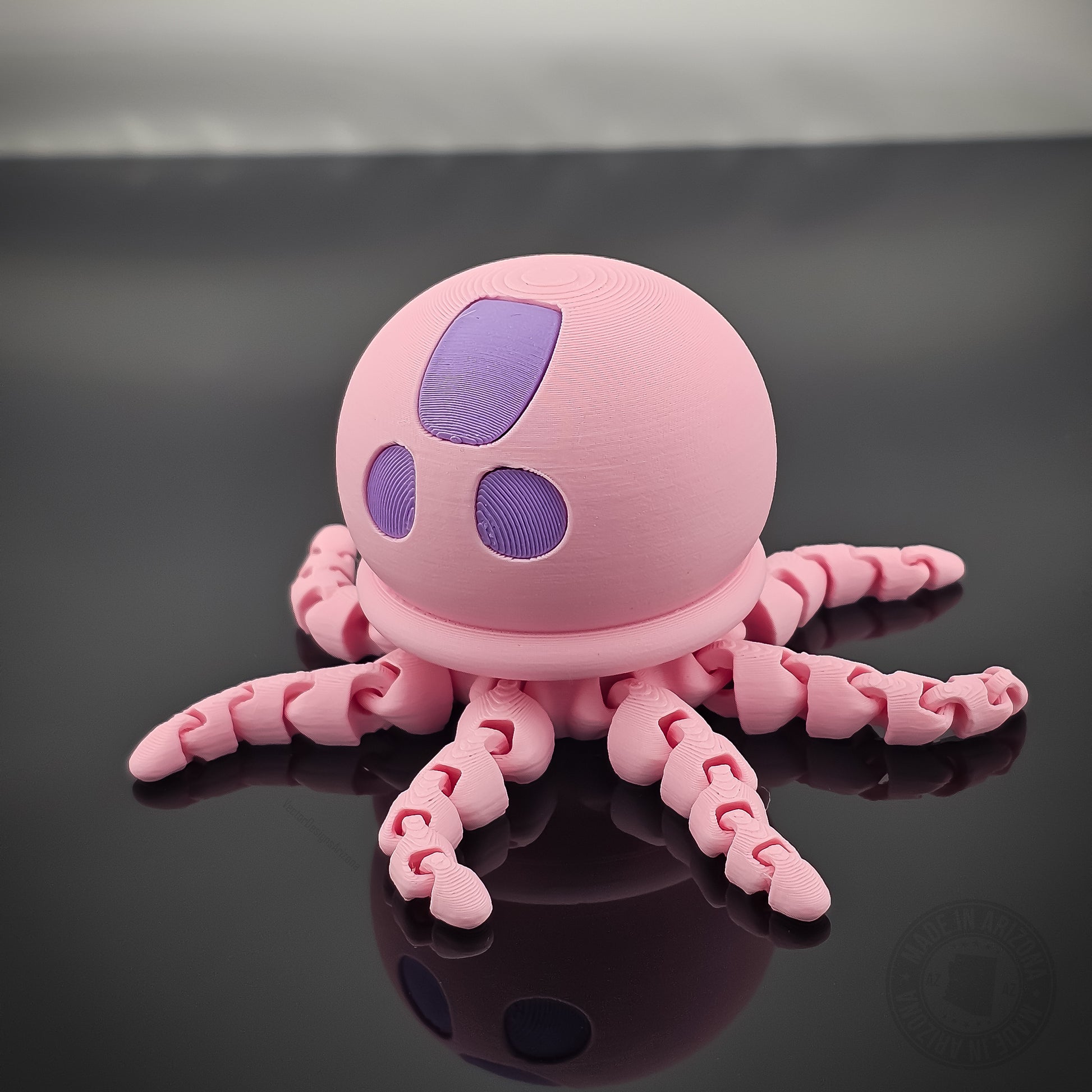 Pink jellyfish flexi fidget toy with tentacles spread out on glossy black surface.