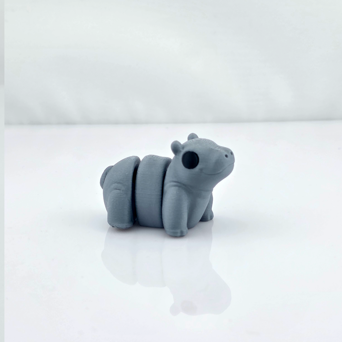 Gray mini flexy hippo toy standing on glossy white background with reflection.