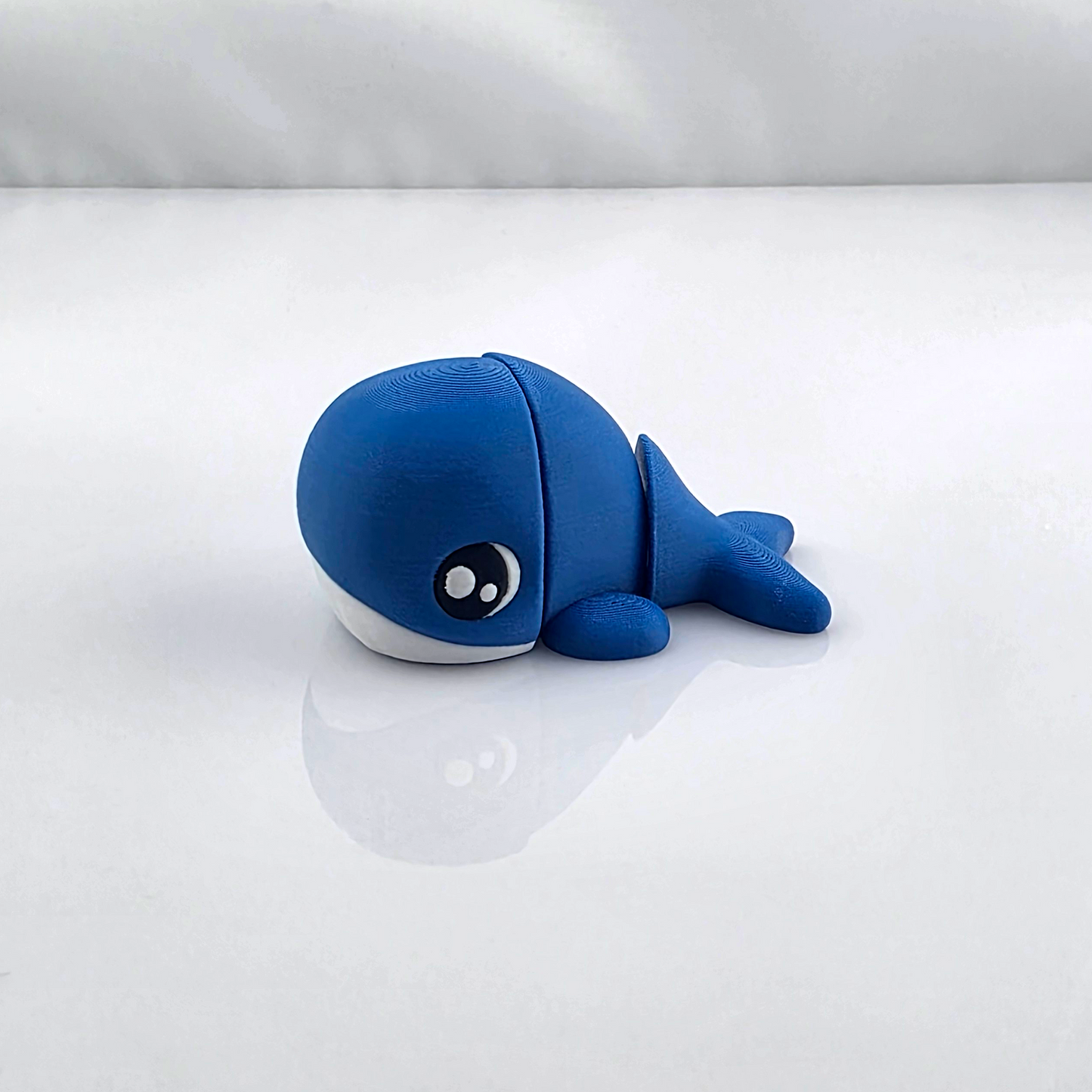 Small blue mini flexy whale toy on white background, shown in side view.