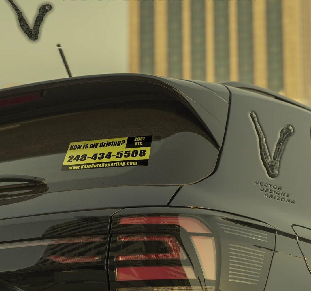 Rick Roll yellow “how is my driving” bumper sticker on rear car window.