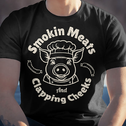 Man wearing black Smokin Meats pig chef barbecue T-shirt outdoors, seated.