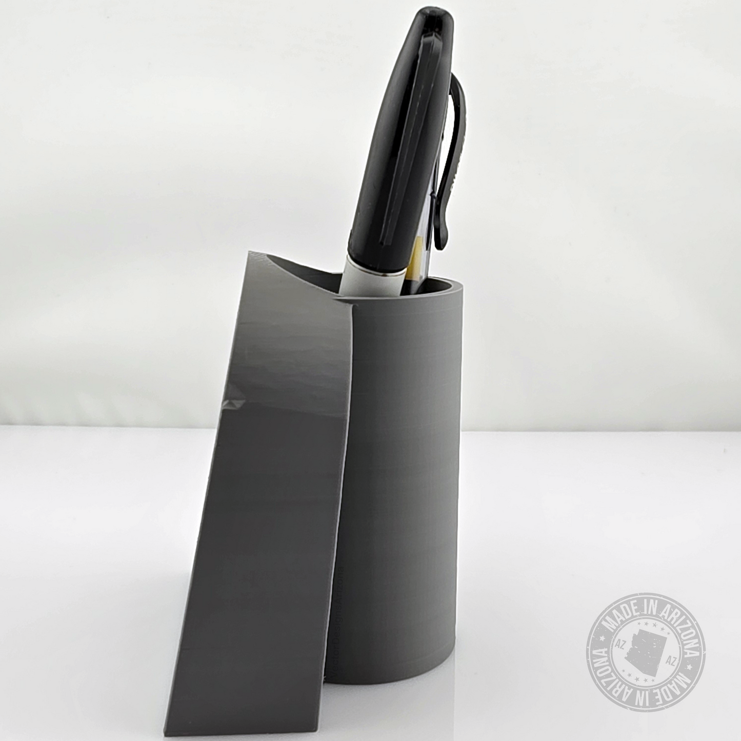 Side profile of gray tombstone desk pen holder with black pens inside.